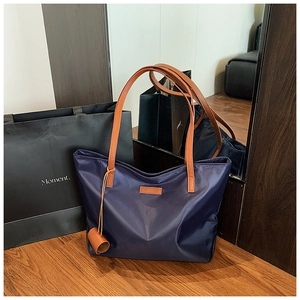 Dettaglio borsa tote in nylon blu navy con manici in pelle marrone su tavolo in legno