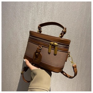Détail du sac cylindrique en toile marron avec bordure en cuir et doubles zips dorés