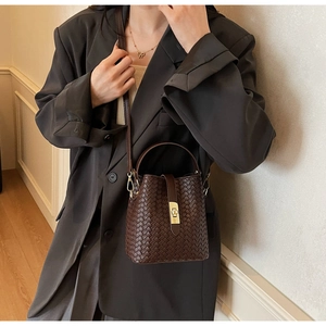 Detail of dark brown woven bucket bag with golden metallic twist lock and handle