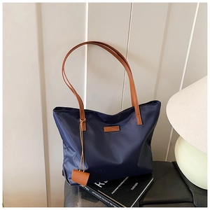 Dettaglio della borsa tote in nylon blu navy con manici in pelle marrone e ciondolo quadrato