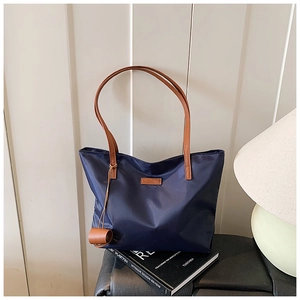 Dettaglio borsa tote blu navy con manici in pelle marrone e toppa frontale con marchio