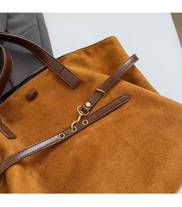 Close-up of brown suede tote bag featuring brass hardware and leather strap details