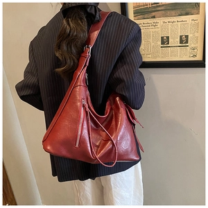 Detail of red textured leather shoulder bag showing wide strap and silver zipper accents
