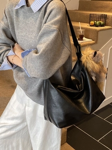 Grand sac bandoulière en similicuir noir avec charme en peluche porté par un mannequin