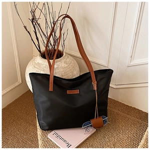 Dettaglio borsa tote in nylon nero con manici in pelle marrone e patch del marchio