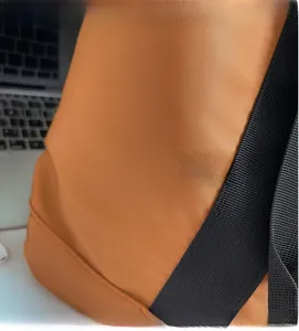 Detail of orange-brown twill fabric texture and reinforced nylon strap stitching on bag