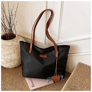Dettaglio della borsa tote in nylon nero con manici in pelle marrone e occhiali da sole