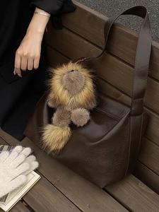 Sac bandoulière vintage marron foncé avec charm lion sur un banc en bois d'extérieur