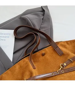 Detail of brown suede tote bag featuring leather handles and decorative metal hardware