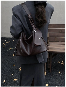 Detail view of deep brown leather tote bag with adjustable strap and small charm pouch