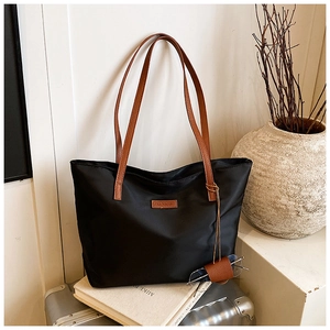 Dettaglio della borsa tote in nylon nero con manici in pelle marrone e logo