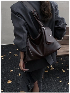 Detail of soft dark brown leather shoulder bag with side zip and rivet on a model
