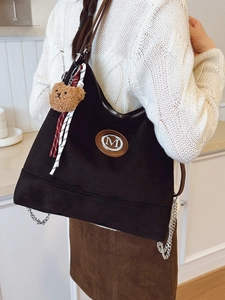 Grand sac cabas noir en daim avec badge M et breloque ours, porté par mannequin