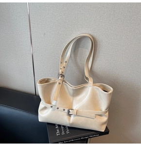 Detail der cremefarbenen Ledertasche mit Zierschnallen auf Büchern platziert