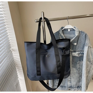 Close-up of a large navy canvas tote bag with black straps and metal snap button pocket