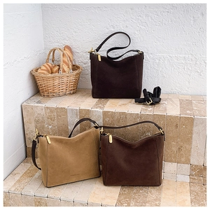 Detailed view of suede tote bags with golden hardware and brand logo on a stone display
