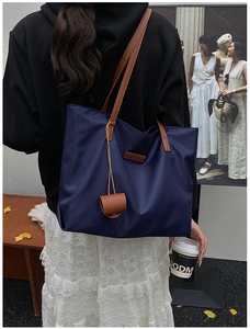 Dettaglio della borsa tote in nylon blu navy con manici marroni e ciondolo decorativo