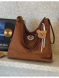 Sac cabas en daim marron avec logo M en métal et breloque ours sur surface en pierre