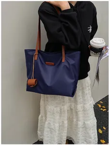 Dettaglio della borsa tote in nylon blu navy con manici in pelle marrone indossata all'aperto
