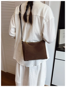 Detail of dark brown suede bucket bag with gold zipper and adjustable shoulder strap
