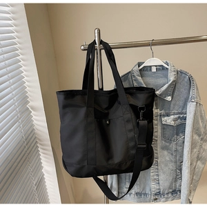 Detail of black canvas tote bag showing wide handles and adjustable woven shoulder strap