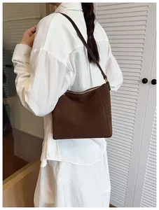 Deep brown suede bucket bag with thin shoulder strap shown in a real-life carrying view