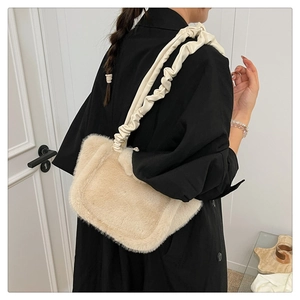 Detail of plush cream faux fur shoulder bag with a ruched strap worn over a black coat