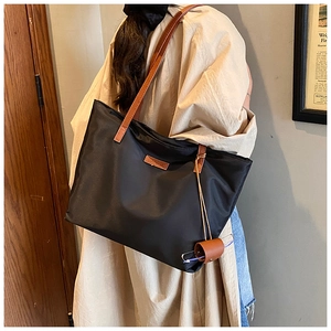 Dettaglio di una borsa tote grande in nylon nero con manici marroni e astuccio appeso