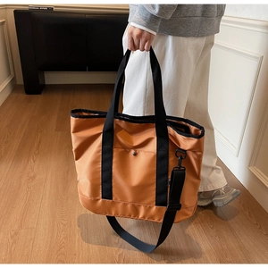 Detail of orange canvas tote bag with black handles and adjustable shoulder strap