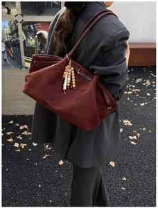 Detail der burgunderroten Wildledertasche mit Holzperlenanhänger auf grauem Blazer