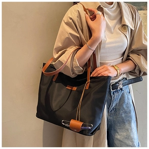 Dettaglio della borsa tote in nylon nero con manici in pelle marrone e clip porta occhiali