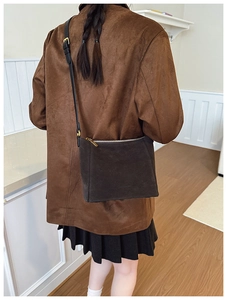 Macro detail of dark brown suede shoulder bag with gold zipper and minimalist design