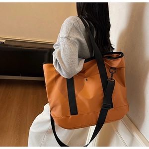 Detailed side view of orange canvas tote bag with black handles and adjustable strap