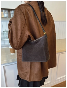Detail of deep brown suede bucket bag with gold hardware and black slim shoulder strap