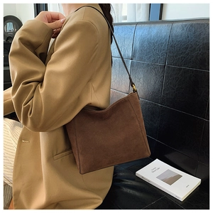 Detail of dark brown suede shoulder bag with gold hardware worn by a model in a blazer
