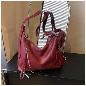 Detail of burgundy leather shoulder bag with silver hardware and heart charm pendant