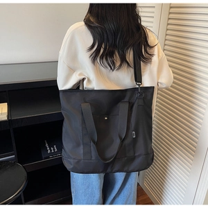 Rear view of a large black canvas tote bag with adjustable straps on a model