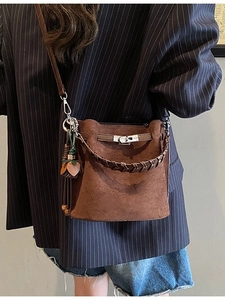 Brown suede bucket bag with woven handle and metal buckle shown on a female model