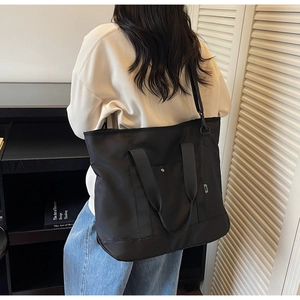 Rear view of model wearing a large black canvas tote bag in a minimalist study room