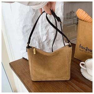Close-up of brown suede bucket bag with gold hardware and brand logo on wooden table