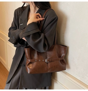 Nahaufnahme einer dunkelbraunen Ledertasche mit Ösengürtel und Schnalle an einem Modell
