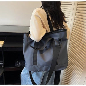 Model view of a large dark grey canvas tote bag with black straps in a modern room