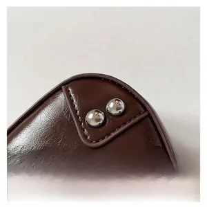 Detail of dark brown saddle bag featuring stitching and silver metallic rivets