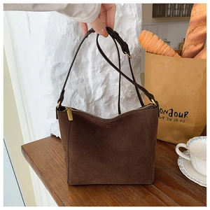Detail of dark brown suede tote bag with metal zipper and adjustable strap in minimalist setting