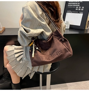 Brown suede tote bag detail featuring MIAOSHE logo embossing and ethnic beaded charm