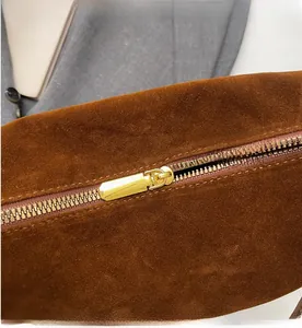 Detailed close-up of smooth gold metal zipper on premium brown suede leather bag