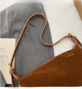 Detail of brown suede shoulder bag with adjustable leather strap and gold zipper hardware
