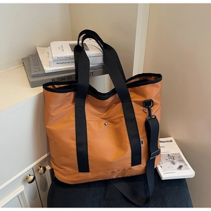 Detail of orange canvas tote bag with adjustable shoulder strap on a black fabric seat