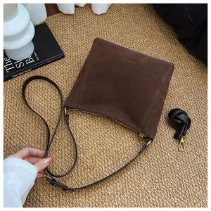 Close-up of brown suede bucket bag with adjustable strap and golden zipper on woven rug