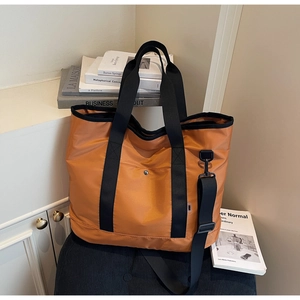 Detail of orange canvas tote bag with metal buckle pocket and black wide shoulder strap